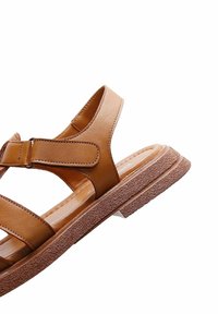 Sandale en cuir marron avec bride de cheville ajustable et semelle en caoutchouc texturée, vue de profil sur fond blanc.