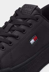 Baskets en cuir noir avec lacets noirs, détails cousus et logo Tommy Jeans en rouge, blanc et bleu sur le panneau latéral.
