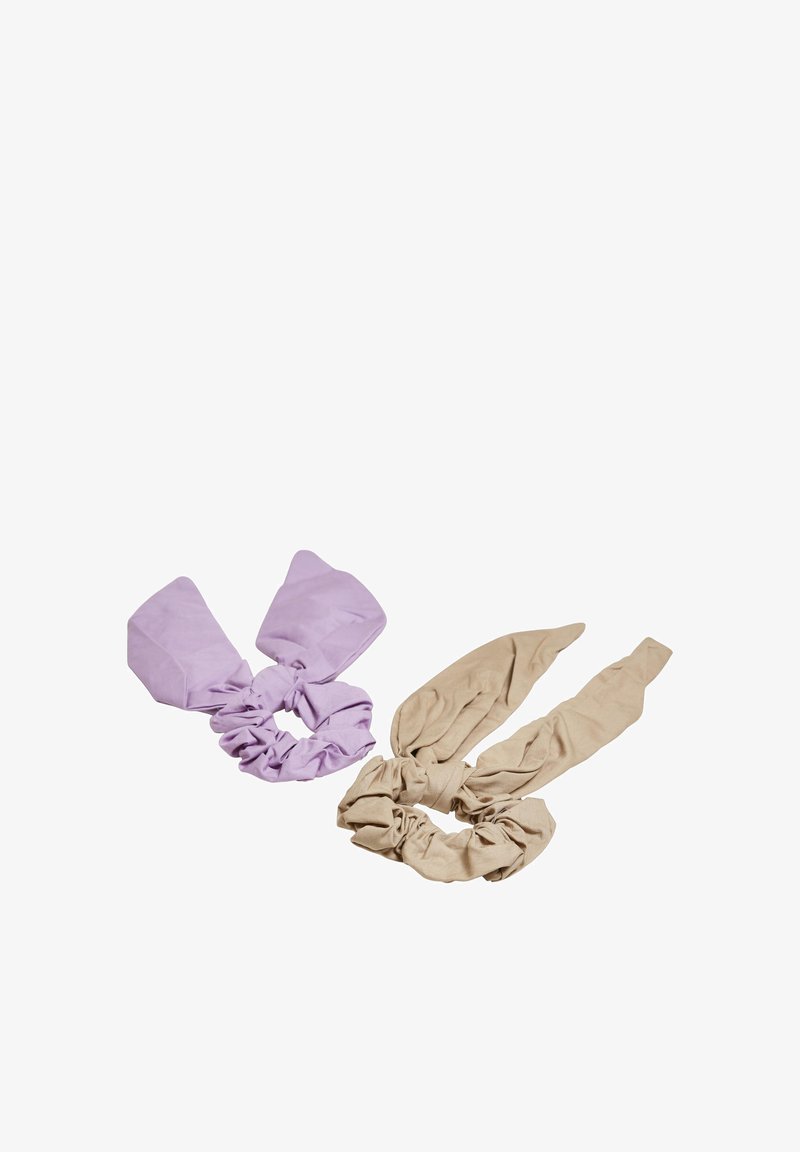 To stof scrunchies med fastgjorte sløjfe-lignende bånd, en i lys lilla og den anden i beige, vist på en hvid baggrund.