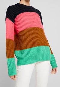 Pull en maille à col rond avec des rayures rose, noir, marron et menthe. Texture côtelée, coupe ample, manches longues avec larges poignets.