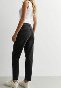 Zwarte denim high-waisted jeans met een relaxte pasvorm, voorzien van achterzakken en gestikte details, gecombineerd met witte sneakers en een aansluitend tanktop.