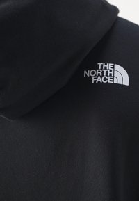 Tissu de sweat à capuche noir avec le logo blanc The North Face sur le haut du dos près de la capuche.