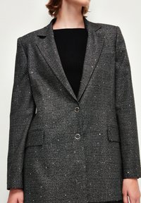 Blazer grigio a quadri con un design strutturato, due bottoni e decorazioni. Presenta rever a lama, tasche a pattina e una texture liscia.