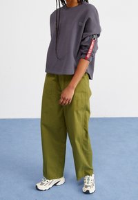 Šedá krátká mikina s rozepínacími rukávy a červenými detaily, kombinovaná s volnými olivově zelenými kalhotami a bílými teniskami s šedými detaily.