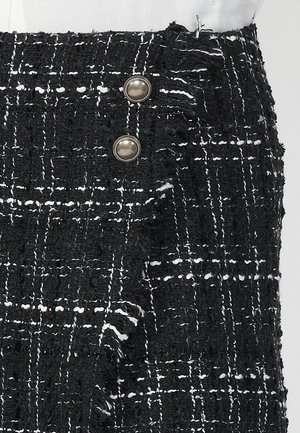 Gonna in tweed bianco e nero con motivo testurizzato, orlo sfrangiato e due bottoni in tonde argento sul lato per la chiusura.