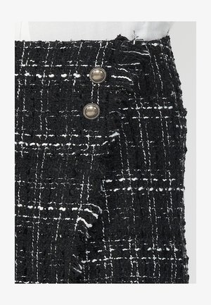Črna in bela tartan krila z teksturiranim vzorcem, razrahljan rob in zaponka z dvema gumboma srebrne barve ob strani.