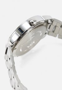 Montre en acier inoxydable argenté avec une surface lisse et polie, un boîtier rond, une couronne texturée et un bracelet en maillons en métal brossé.