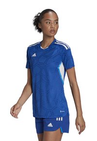 Maglia atletica blu con un motivo geometrico, maniche corte e scollatura a V, abbinata a pantaloni blu e logo Adidas bianco.