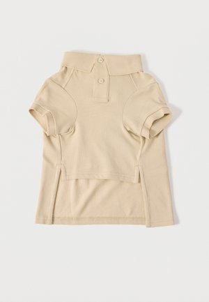 Polo beige à manches courtes avec deux boutons, col côtelé et fentes latérales, posé à plat sur un fond clair.