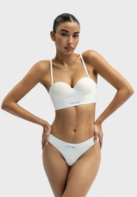 White padded bralette with adjustable straps, paired with a matching thong. Smooth fabric, minimalist design, featuring a label at the front.
