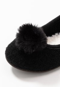 Ciabatta nera con esterno in lana a trama, decorata con un soffice pompon nero sulla punta, e con un morbido interno simil-pelliccia bianca.