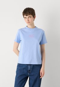 Vaaleansininen puuvillapaita, jossa on pyöreä pääntie ja lyhyet hihat. Paidassa on keskellä vaaleanpunainen Calvin Klein -logo.