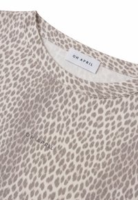 Gros plan d'une chemise en tissu beige et marron clair à pois, col rond avec "OH APRIL" imprimé près du col et de la poitrine.