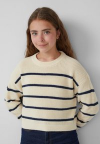 Crème trui met marineblauwe horizontale strepen, gebreide textuur, ronde hals en verlaagde schouders, gecombineerd met donkere jeans.