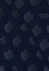 Mørk navy stof med teksturerede, lagdelte blomster i en let mørkere nuance, prydet med centre af intrikate detaljer.