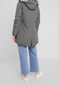 Szara pikowana kurtka z kapturem wykończonym sztucznym futrem w panterkę, zapinana na zatrzaski, z bocznymi rozcięciami, noszona na szerokich dżinsach i białych tenisówkach.