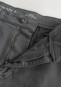 Temno sive tehnične hlače z zadrgo spredaj, zapiranjem na gumbe in teksturiranim pasom. Izdelane so iz gladkega tkanega materiala s čistimi šivi.