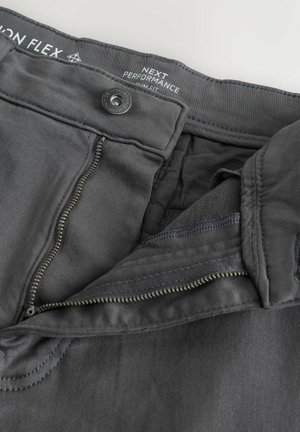 Dunkelgraue Performance-Hose mit Reißverschluss, Knopfverschluss und strukturiertem Bund. Aus einem glatten Stoff mit sauberen Nähdetails.