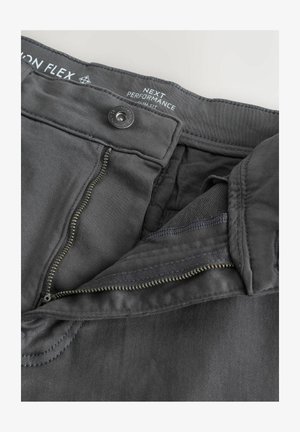 Pantalones de rendimiento gris oscuro con cremallera, cierre de botón y cinturilla texturizada. Presentan una tela suave y detalles de costura limpia.