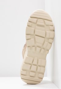 Suela de zapato deportivo beige con un patrón de relieve prominente; material de goma y superficie texturizada; diseñada para tracción y durabilidad.