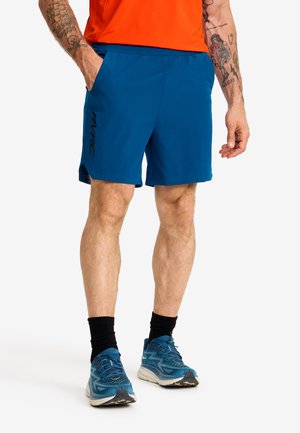 Blå idrottsshorts har en elastisk midja, sidofickor och en logotyp på vänster ben. Bärs med blå löparskor och svarta strumpor.