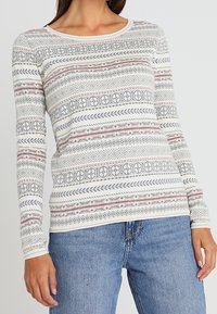 Camisa de manga larga en color crema con patrones geométricos en rosa, azul y gris. Presenta un escote redondo y un diseño ajustado. Textura de tela suave.