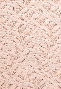 Záběr zblízka na růžovou tkaninu s copánkovými a zkroucenými vzory vytvářejícími texturovaný diagonální design.