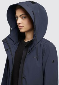Jacket a cappuccio blu navy realizzata in tessuto morbido e resistente all'acqua, con chiusure a zip e a bottone; presenta un cappuccio regolabile e un dettaglio del logo.