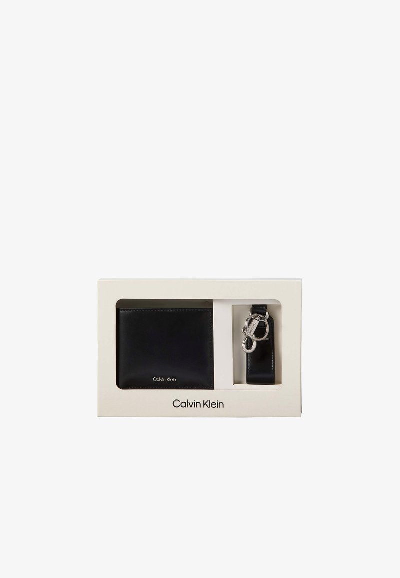 Μαύρο δερμάτινο πορτοφόλι και μπρελόκ Calvin Klein με μεταλλικά κλιπς σε λευκό ορθογώνιο κουτί δώρου.