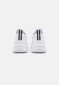 Tenis brancos com uma plataforma texturizada, apresentando uma faixa vertical preta no calcanhar e uma marcação em relevo na sola. Design limpo.