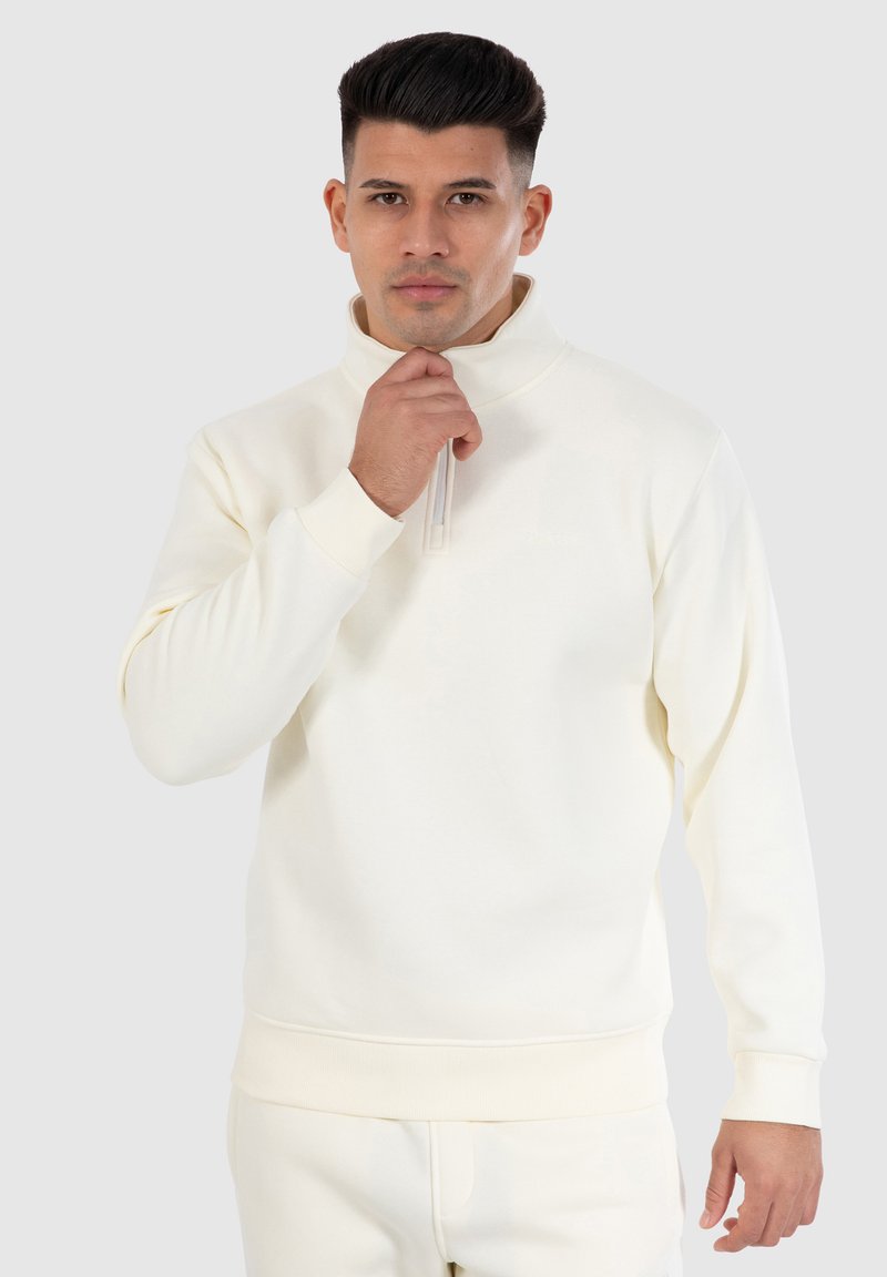 Crème-kleurige pullover van zachte stof met een hoge kraag, halve rits en ribgebreide manchetten en zoom. Bevat subtiele branding.