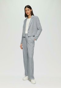 Lichtgrijze double-breasted blazer met metallic knopen, gecombineerd met bijpassende hoge taille broek en witte sneakers. Zachte stoftextuur.