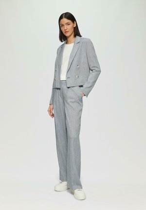 Lichtgrijze double-breasted blazer met metallic knopen, gecombineerd met bijpassende hoge taille broek en witte sneakers. Zachte stoftextuur.