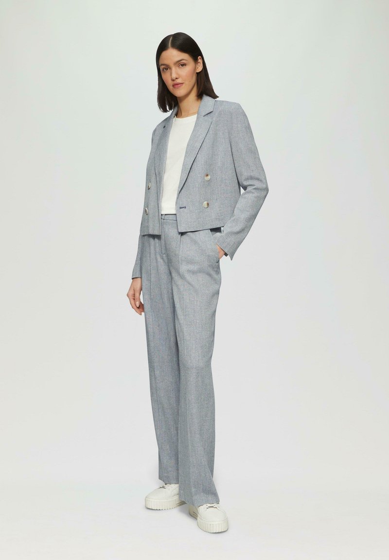 Lichtgrijze double-breasted blazer met metallic knopen, gecombineerd met bijpassende hoge taille broek en witte sneakers. Zachte stoftextuur.