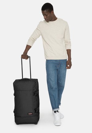 Black rolling suitcase made of durable fabric, with a rectangular shape, side buckles, and a telescoping handle for easy transport.