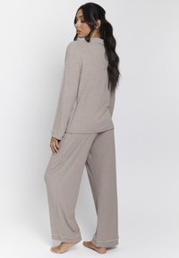 Conjunto de pijama de manga larga en color beige, de tela suave, que incluye pantalones de pierna ancha, un corte relajado y ribetes blancos en las mangas y el dobladillo de los pantalones.