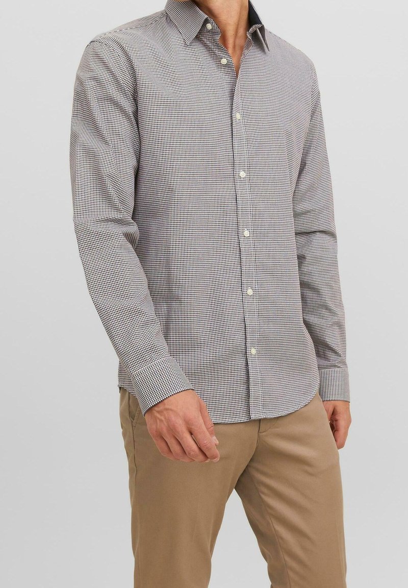 Mans långärmad skjorta i ett litet rutmönster, främst vit och marinblå, med knappad krage och standardmanschetter. Tillverkad av bomull.