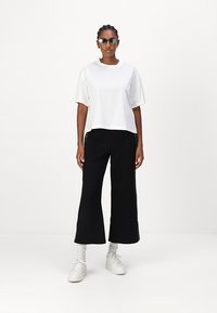 Fehér rövid ujjú crop top fekete, széles szárú nadrággal, oldalpanel részletekkel, fehér sportcipőkkel és napszemüveggel párosítva.