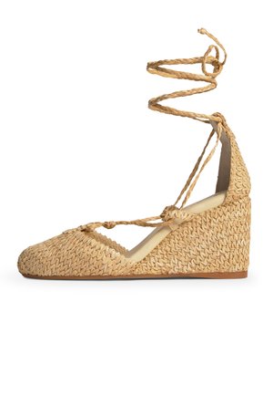 Zapato de cuña con textura de paja tejida, punta cerrada, cordones trenzados hasta el tobillo y suela de goma color marrón claro.