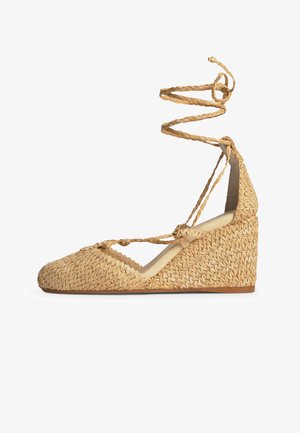 Zapato de cuña con textura de paja tejida, punta cerrada, cordones trenzados hasta el tobillo y suela de goma color marrón claro.