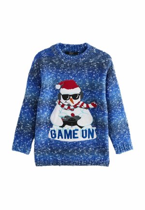 Niebieski sweter w plamki z bałwankiem w okularach przeciwsłonecznych, słuchawkach, czerwonej czapce Mikołaja, czerwonym szaliku, trzymającym kontroler do gry z napisem "GAME ON".