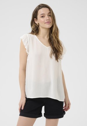 Blouse blanche légère avec un décolleté en V et des manches à volants. Texture douce, légèrement transparente avec des rayures verticales. Portée avec un short noir retroussé.