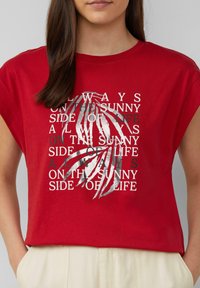 Rode t-shirt met korte mouwen, afgewerkt met een grafische print in zilver en zwart, met gestileerde tekst en palmbladeren. Katoenen materiaal, relaxed fit.