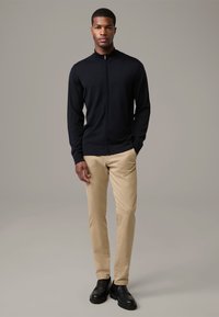 Marinefarbener Zip-Up-Pullover mit Kragen, kombiniert mit beigen Hosen und schwarzen Schuhen. Geschmeidige Textur, figurschmeichelnder Schnitt und lässiger Stil.