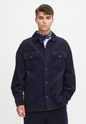Navy corduroy shirt jacket with two front pockets, button closure, and a spread collar. Textured fabric with vertical ribbing, casual fit.