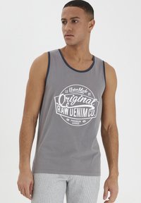 Szürke, ujjatlan tank top, kerek, fehér grafikával, amely a "Original Raw Denim Co." feliratot vintage stílusban jeleníti meg. Kontrasztos nyakkivágás szegéllyel.