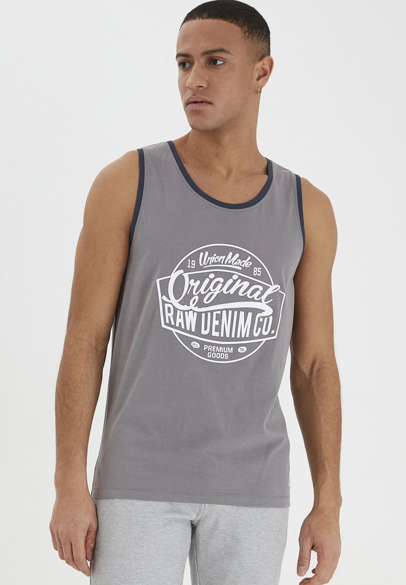 Szürke, ujjatlan tank top, kerek, fehér grafikával, amely a "Original Raw Denim Co." feliratot vintage stílusban jeleníti meg. Kontrasztos nyakkivágás szegéllyel.