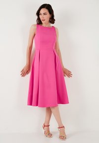 Rochie fără mâneci de culoare fuchsia, cu un corset ajustat și o fustă evazată, având plissuri și o textură netedă. Complementată de sandale cu toc colorate.