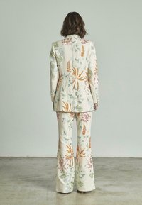 Traje bordado con patrones florales en colores pastel sobre fondo crema; incluye una chaqueta ajustada y pantalones acampanados.