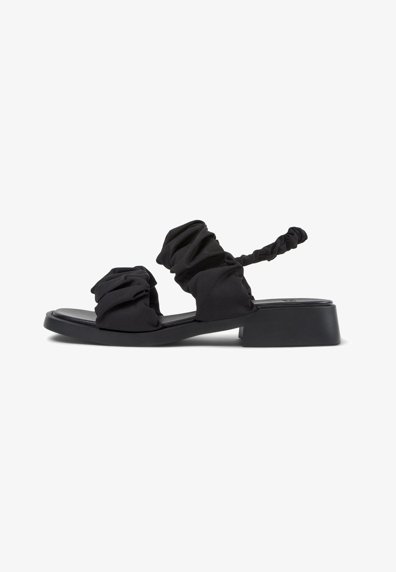 Les sandales noires présentent un design en tissu doux froncé, un bout ouvert, une semelle plate et une bride arrière torsadée pour un ajustement réglable.